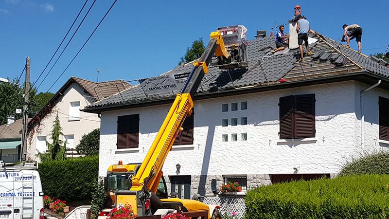 Travaux de réfection de toiture avec couvreurs en action et engin de levage pour poser les nouvelles tuiles.