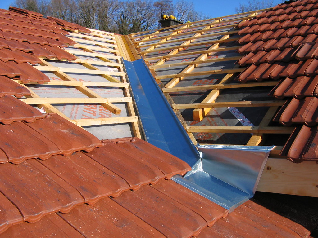 Travaux de couverture avec pose d’une noue en zinc et installation progressive des tuiles sur une toiture.